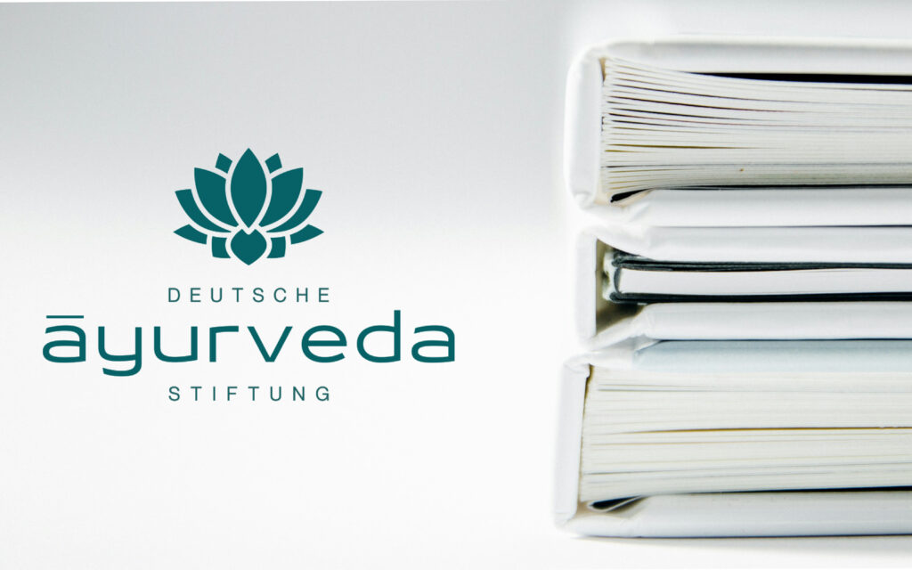 Das Logo der Deutschen Ayurveda Stiftung neben einem Stapel weißer Bücher