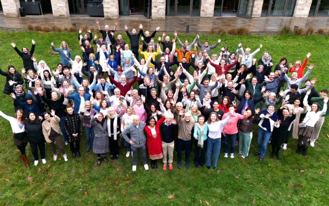 Glückliche Teilnehmer(innen) der Ayurveda Fach-Couch Ausbildung stehen auf einer gründen Rasenfläche und strecken lächelnd die Hände in die Luft.